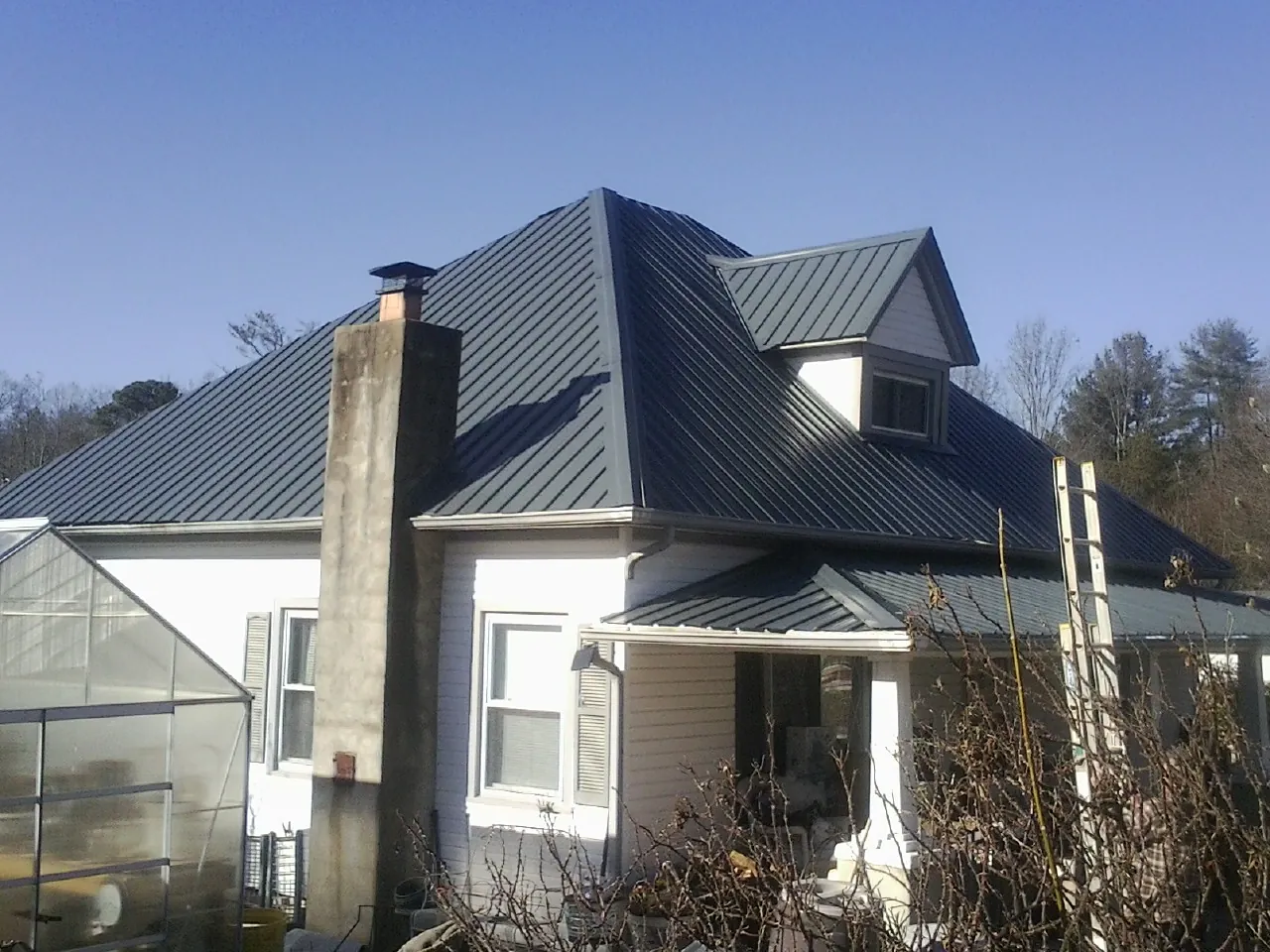 Dark blue standing seam metal roof on a white farmhouse with dormer — Slate & Tile Roof Repair by Roofing Brothers in Waxhaw