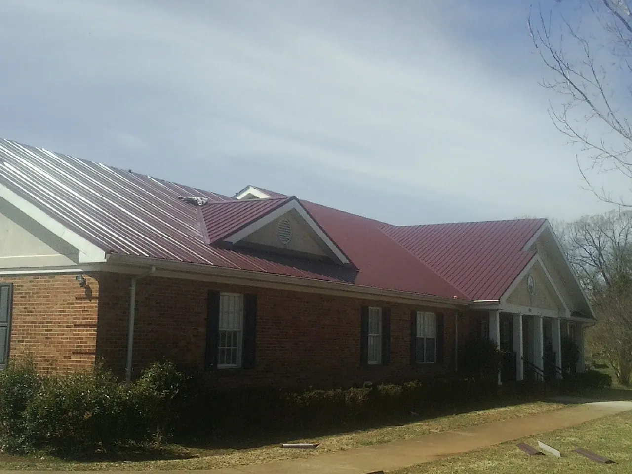 Red metal roof with gabled entries on a long brick building, from a Hail Damage Roof Repair job in Waxhaw
