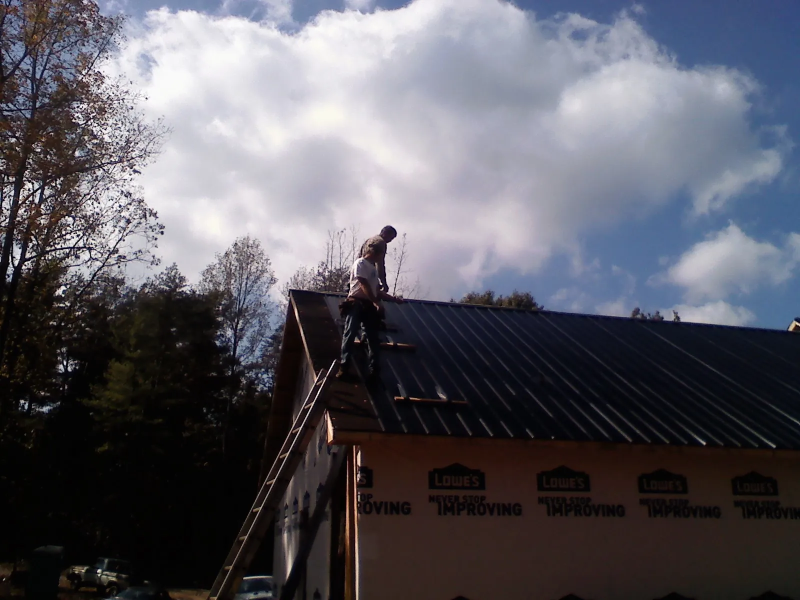 Roofer fastening dark metal panels high against a cloudy sky, from a Roof Inspection job in Waxhaw