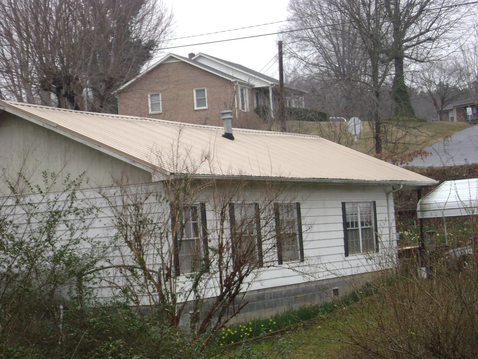 Tan metal roof on a white sided house set into a hillside — Commercial Roofing by Roofing Brothers in Waxhaw